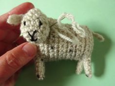 a small crocheted sheep is being held by someone's hand on a green surface