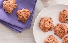 some cookies are on a white plate next to a glass of milk and a purple napkin