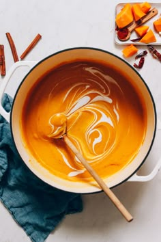 a pot filled with orange liquid next to cinnamon sticks and other ingredients on a white surface