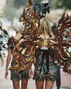 two models walk down the runway in gold and black dresses with intricate designs on them