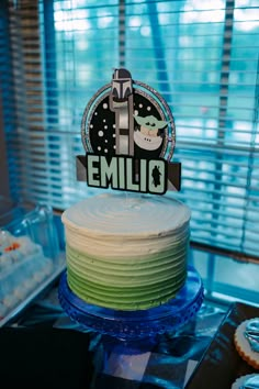 a cake with the name emelio on it sitting in front of some cupcakes