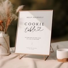 a cookie table sign sitting on top of a table next to a vase with dried flowers