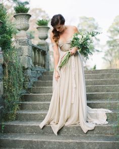 a woman in a long dress is standing on some stairs with flowers and greenery