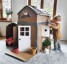 a young boy playing with a cardboard house made to look like it is built into the ground