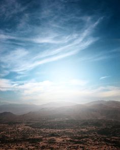 an airplane flying in the sky over a desert area with mountains and clouds behind it