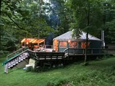 a small wooden cabin in the woods with lights on it's porch and stairs leading up to an upper level deck