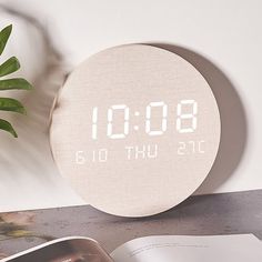 an alarm clock sitting on top of a table next to a book and potted plant