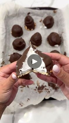 a person holding a piece of chocolate covered in white frosting and sprinkles