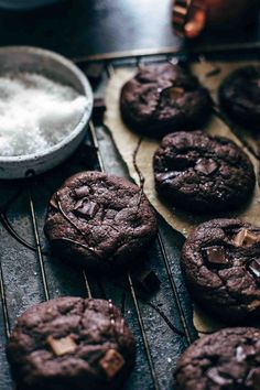 several chocolate cookies cooling on a rack next to a bowl of salt and spoons