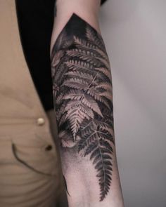 a woman's arm with a black and grey fern tattoo on the left forearm