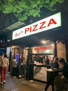 people standing outside of a pizza restaurant at night