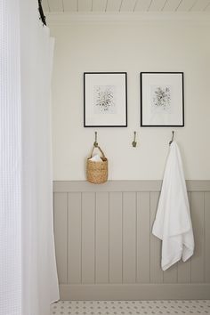 two framed pictures hang on the wall next to a white towel rack and a wicker basket