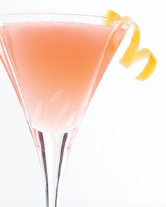 a pink drink in a martini glass garnished with an orange slice