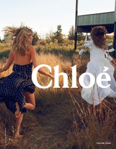 two girls in dresses are running through the grass and one girl is holding her hand out