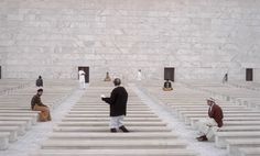 people are sitting on benches in the middle of a large room with white marble walls