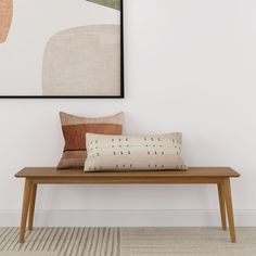 a wooden bench sitting in front of a white wall with a painting on the wall