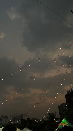 there are many lights strung from the wires in the sky above some tents and buildings