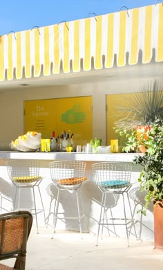 an outdoor bar with yellow and white awnings on the roof, surrounded by potted plants