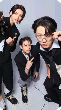 three young men posing for a photo in front of a white background with one pointing at the camera