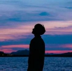 a person standing in front of the water at sunset with their head turned to the side