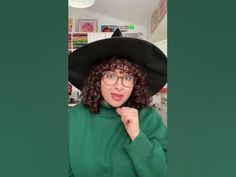 a woman with curly hair wearing a black hat and green sweater is making a funny face