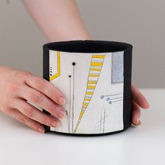 a woman's hand is holding onto a black and white cup with yellow lines on it