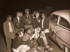 a group of young men standing next to each other near an old car at night