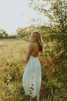 a woman in a white dress standing in tall grass with her back to the camera