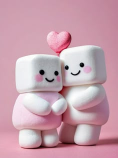 two marshmallows are hugging each other with a pink heart on the top