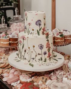 a three tiered wedding cake with flowers on the side and cookies in the background