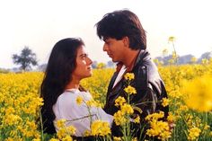 a man and woman standing next to each other in a field full of yellow flowers