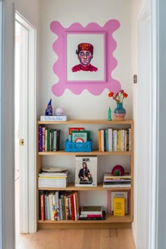 a bookshelf filled with lots of books in front of a painting on the wall