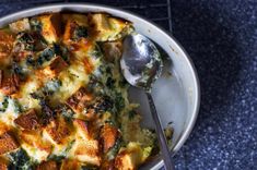 a casserole dish with broccoli and cheese on it, next to a spoon