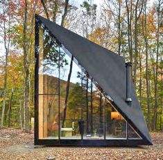 a triangular shaped house in the woods with glass walls and windows on it's side