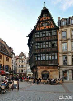 people are sitting at tables in the middle of an old town square with half - timbered buildings