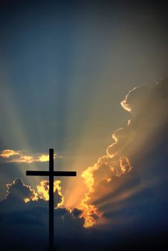 a cross with the sun shining behind it in front of some clouds and blue sky