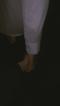 two people holding hands in the dark with one person wearing a white shirt and black pants