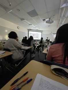 people sitting at desks in a classroom with papers and pens on the desks