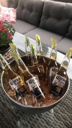 several bottles of alcohol sitting in a metal bowl on a table with flowers and potted plants