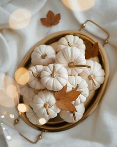 small white pumpkins in a gold bowl on a table with candles and lights around them