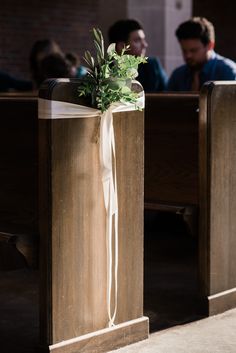 a white ribbon tied to the back of pews with greenery on it and people sitting in the background