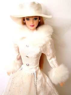 a doll wearing a white dress and hat with fur on it's head, standing next to a wall