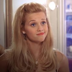 a woman with long blonde hair and blue eyes looks into the distance while sitting in front of a mirror