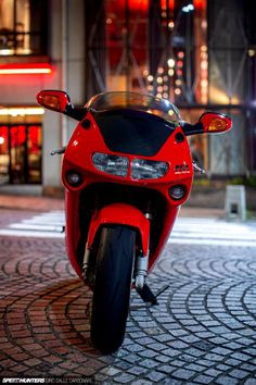 a red motorcycle parked in front of a tall building at night with its lights on