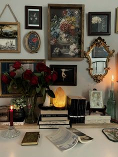 a table topped with books and vases filled with red roses next to framed pictures