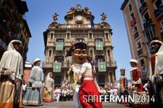 people dressed in costumes are walking down the street with buildings and clock tower behind them