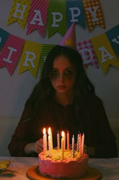 a woman sitting in front of a birthday cake with lit candles on top of it