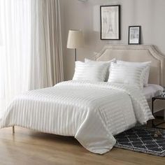 a bed with white sheets and pillows in a bedroom next to a lamp on a table