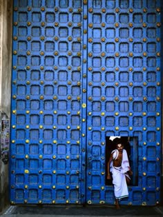 a person standing in front of a blue door with gold studs on the doors