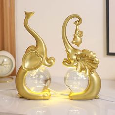 two golden elephants are standing next to each other on a white table with a clock in the background